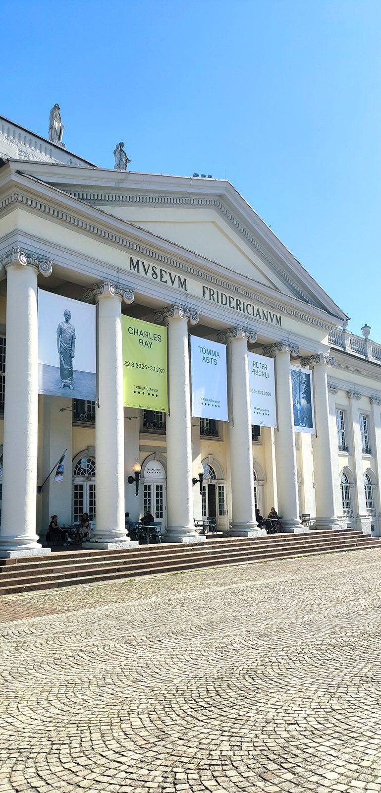 Ausstellungsbanner zwischen den Säulen des Museum Fridericianum in Kassel, Hochformat