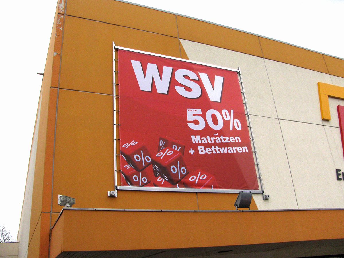 Roter Fassadenbanner in einem Metallrahmen mit Kederschienen an der Fassade eines Möbelhauses