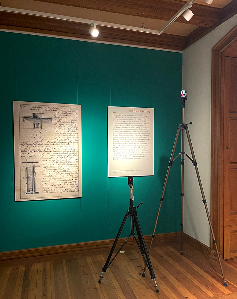 Hartschaumplatte mit historischer Handschrift neben einer Texttafel an einer grünen Museumswand